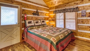 A cozy cabin-style room with a wooden ceiling, a bed with a quilt, a fire extinguisher, and a window with blinds. - Linger Longer 1607 - One Bedroom Cabin (Gatlinburg)