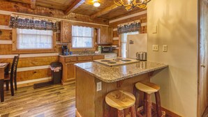 A kitchen with wooden cabinets, a granite countertop, a built-in stove, and a chandelier. - Linger Longer 1607 - One Bedroom Cabin (Gatlinburg)