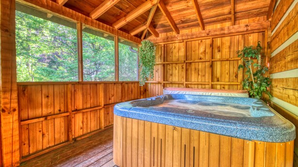 Una cabaña de madera con jacuzzi, ventanas amplias y una terraza de madera.