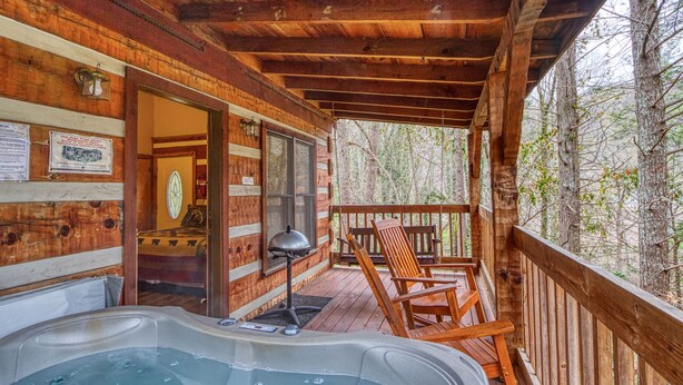 A wooden cabin with a hot tub, wooden deck, and a view of the forest. - Puppy Love 1619 - One Bedroom Cabin (Gatlinburg)