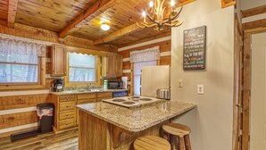 A kitchen with wooden walls, a granite countertop, and a chandelier. - Puppy Love 1619 - One Bedroom Cabin (Gatlinburg)