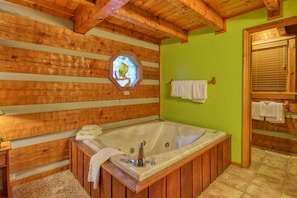 A wooden cabin-style bathroom with a large bathtub, wooden beams, and a green wall. - Parkside Party 1676 - One Bedroom Cabin (Gatlinburg)