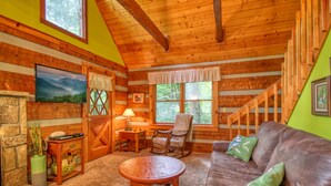 A cozy cabin interior with a wooden ceiling, a fireplace, a sofa, and a dining area. - Parkside Party 1676 - One Bedroom Cabin (Gatlinburg)