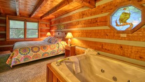 A cozy cabin room with a bed, a bathtub, and a window with a wooden ceiling. - Parkside Party 1676 - One Bedroom Cabin (Gatlinburg)