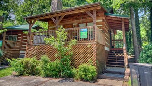 A rustic wooden cabin with a covered porch and a chimney, surrounded by lush greenery. - Cuddle Inn 1529 - One Bedroom Cabin (Gatlinburg)
