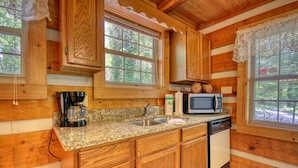 A wooden cabin kitchen with granite countertops, a sink, a coffee maker, a microwave, and a dishwasher. - Cuddle Inn 1529 - One Bedroom Cabin (Gatlinburg)