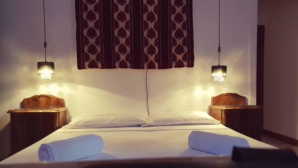 A neatly made bed with white linens and two rolled towels, flanked by wooden nightstands with lamps. - Casa Di Adel (Venice)