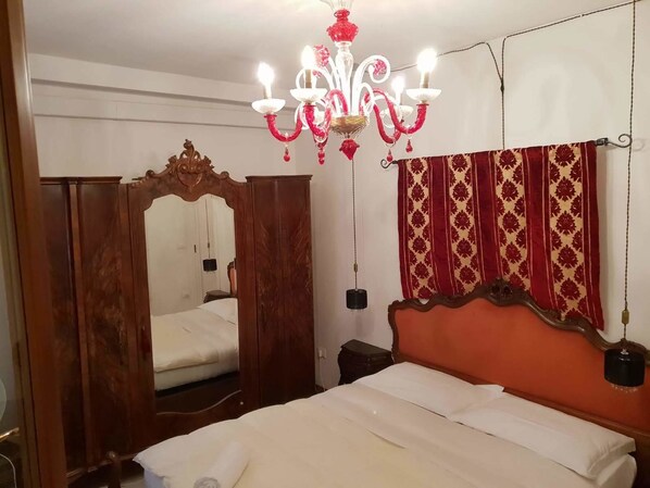 A bedroom with a wooden wardrobe, a bed with white bedding, a red and gold patterned curtain, and a chandelier. - Casa Di Adel (Venice)