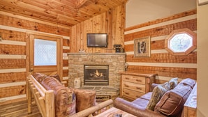 A log cabin interior with a stone fireplace, wooden furniture, and a television mounted above it. - Leather And Lace 1615 - One Bedroom Cabin (Gatlinburg)