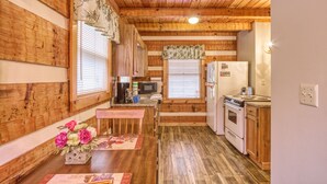 A wooden cabin interior with a kitchen area featuring a stove, microwave, refrigerator, and wooden cabinets. - Leather And Lace 1615 - One Bedroom Cabin (Gatlinburg)