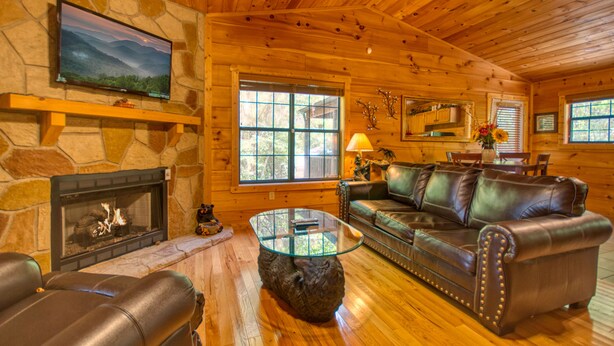 A log cabin interior with a stone fireplace, leather furniture, and large windows. - Dream Maker 120 - One Bedroom Cabin (Sevierville)