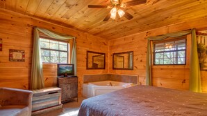 A wooden cabin bedroom with a bed, a vanity with a mirror, a bathtub, and a ceiling fan. - Dream Maker 120 - One Bedroom Cabin (Sevierville)