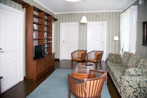 A living room with a wooden bookshelf, a television, a sofa, and a dining table with chairs. - Tehtaan Hotelli (Karkkila)