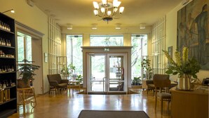 A spacious lobby with a wooden floor, a reception desk, and a large window offering a view of greenery outside. - Tehtaan Hotelli (Karkkila)