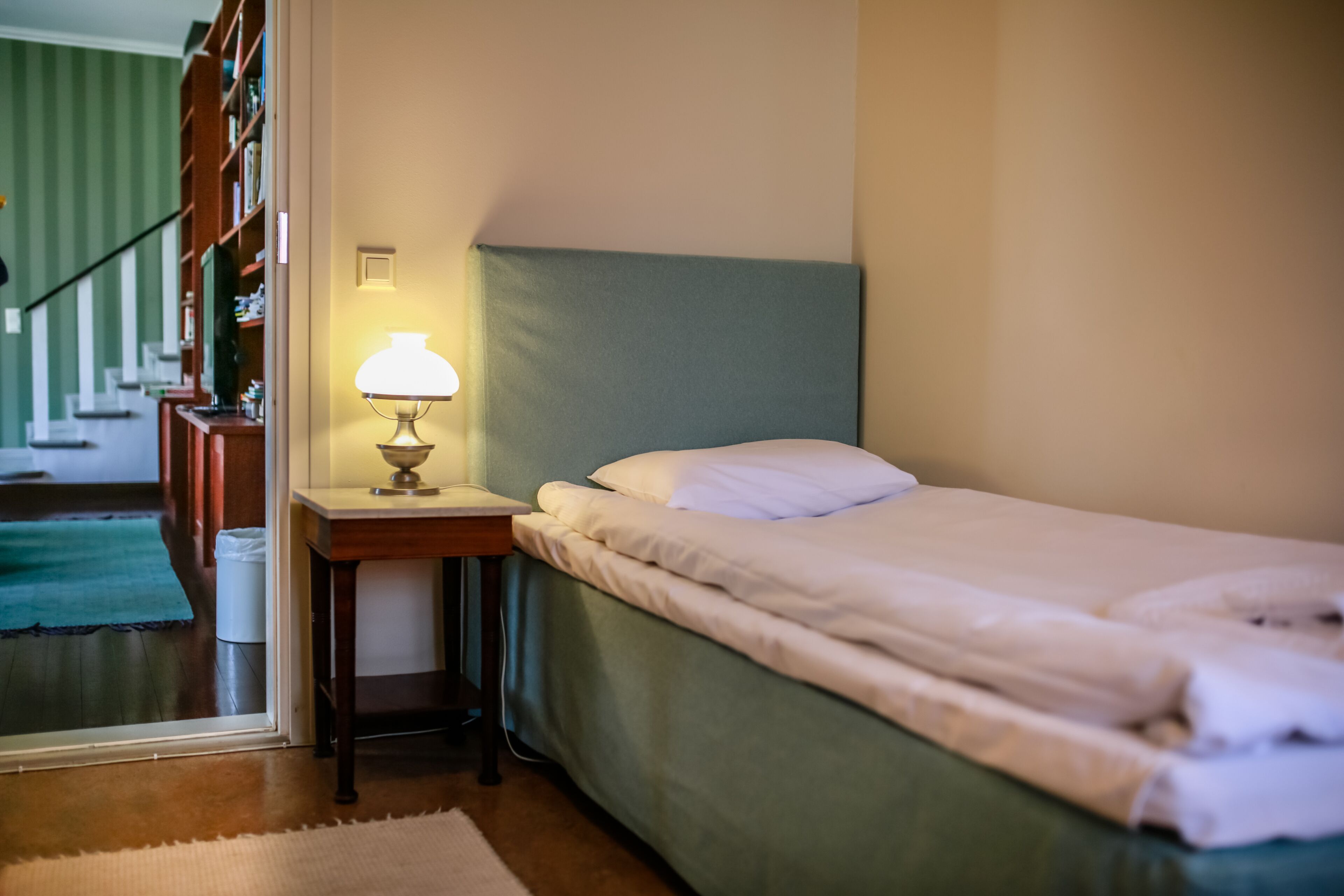 Un dormitorio con una cama, una mesita de noche con una lámpara, un cabecero verde y vistas a una escalera.