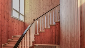A wooden staircase with a black handrail leading to a landing. - Tehtaan Hotelli (Karkkila)