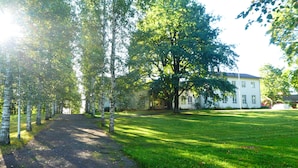 A pathway lined with birch trees leading to a white building with multiple windows. - Tehtaan Hotelli (Karkkila)