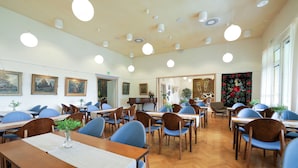 A dining area with multiple tables and chairs, a wooden floor, and ceiling lights. - Tehtaan Hotelli (Karkkila)