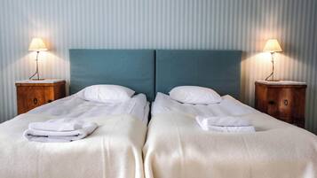 A hotel room with two beds, each with a white bedspread and pillows, flanked by wooden nightstands with lamps.