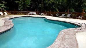 Una piscina con borde de piedra, rodeada de sillones y mesas, con una valla de madera y árboles al fondo.