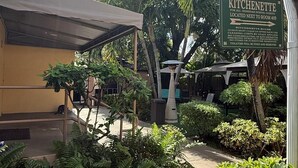Un cortile con un cartello per la kitchenette, un'area salotto coperta e una vegetazione rigogliosa.