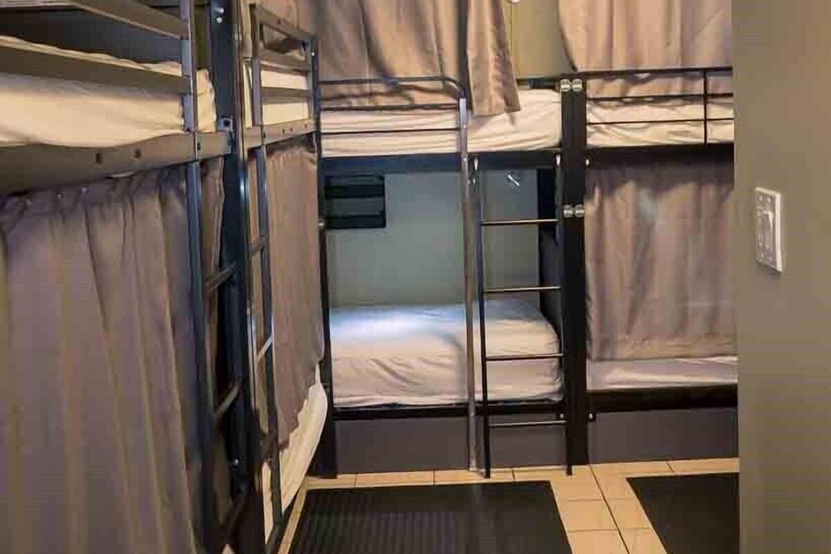 A dormitory room with bunk beds, a small desk, and a window with curtains.