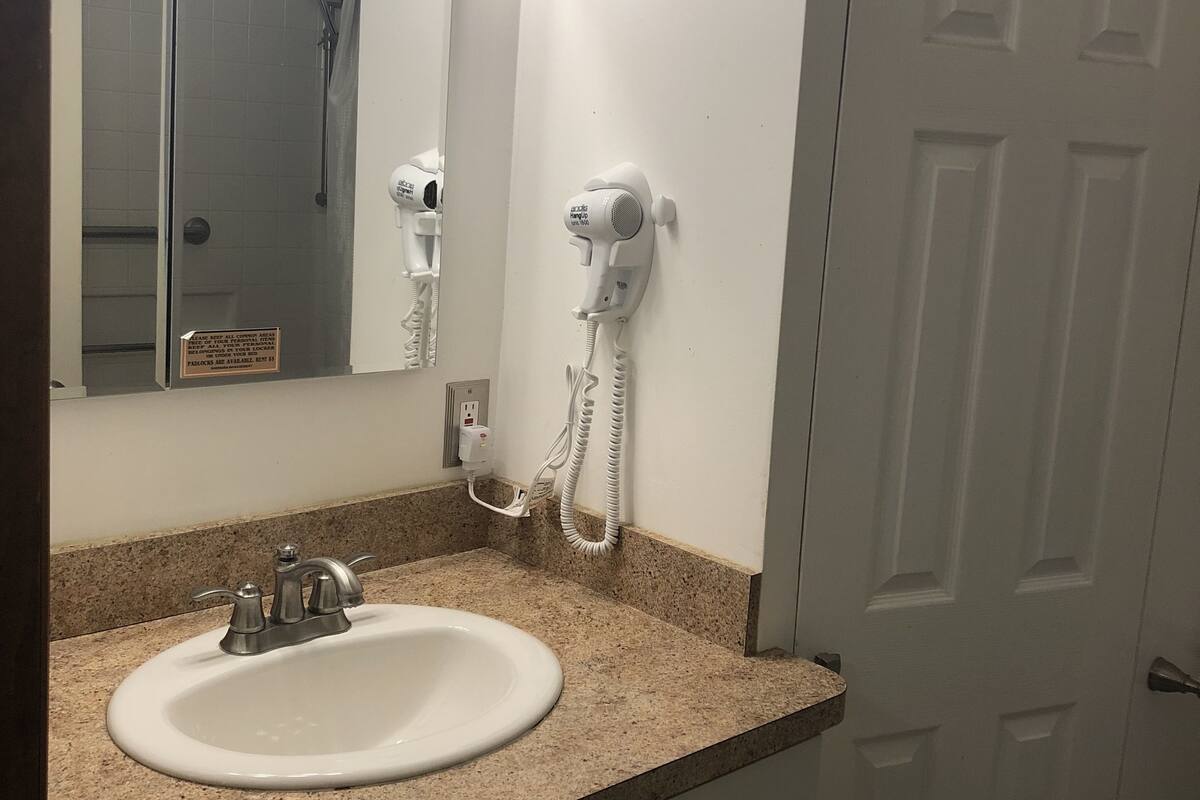 A bathroom with a sink, mirror, hairdryer, and a door.