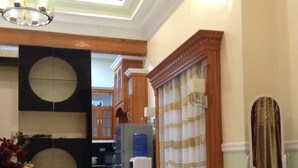 A hallway with a chandelier, a large mirror, and a decorative vase with flowers. There is a refrigerator and a water dispenser in the background. - DanSam House (Davao)