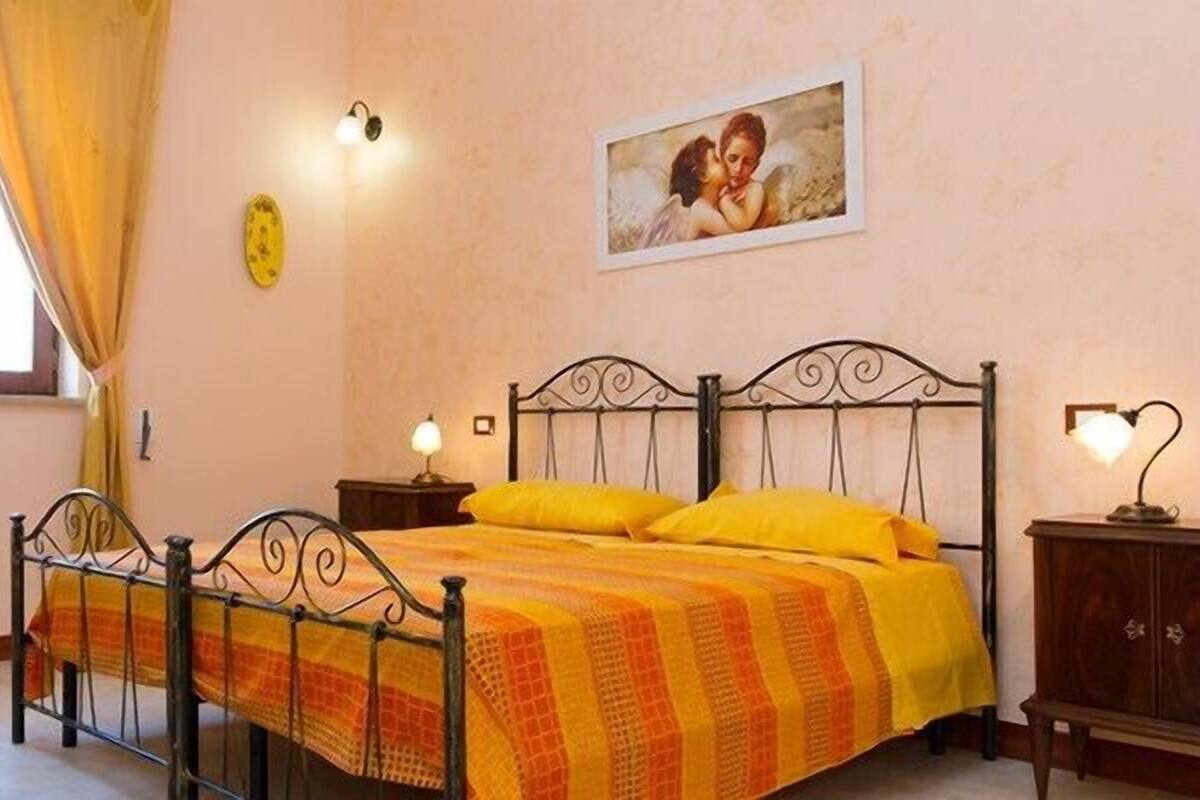 Un dormitorio con cama, mesita de noche, silla, ventana con cortinas e imagen colgada en la pared.