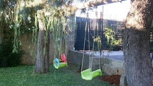 A backyard with a swing set, a small tree, and a stone wall. - B&B Li Cuti (Tiggiano)