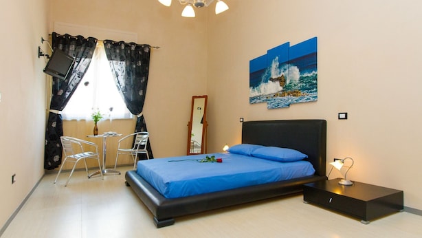 A bedroom with a bed, a nightstand, a desk with a chair, a mirror, and a painting of a seascape. - B&B Li Cuti (Tiggiano)