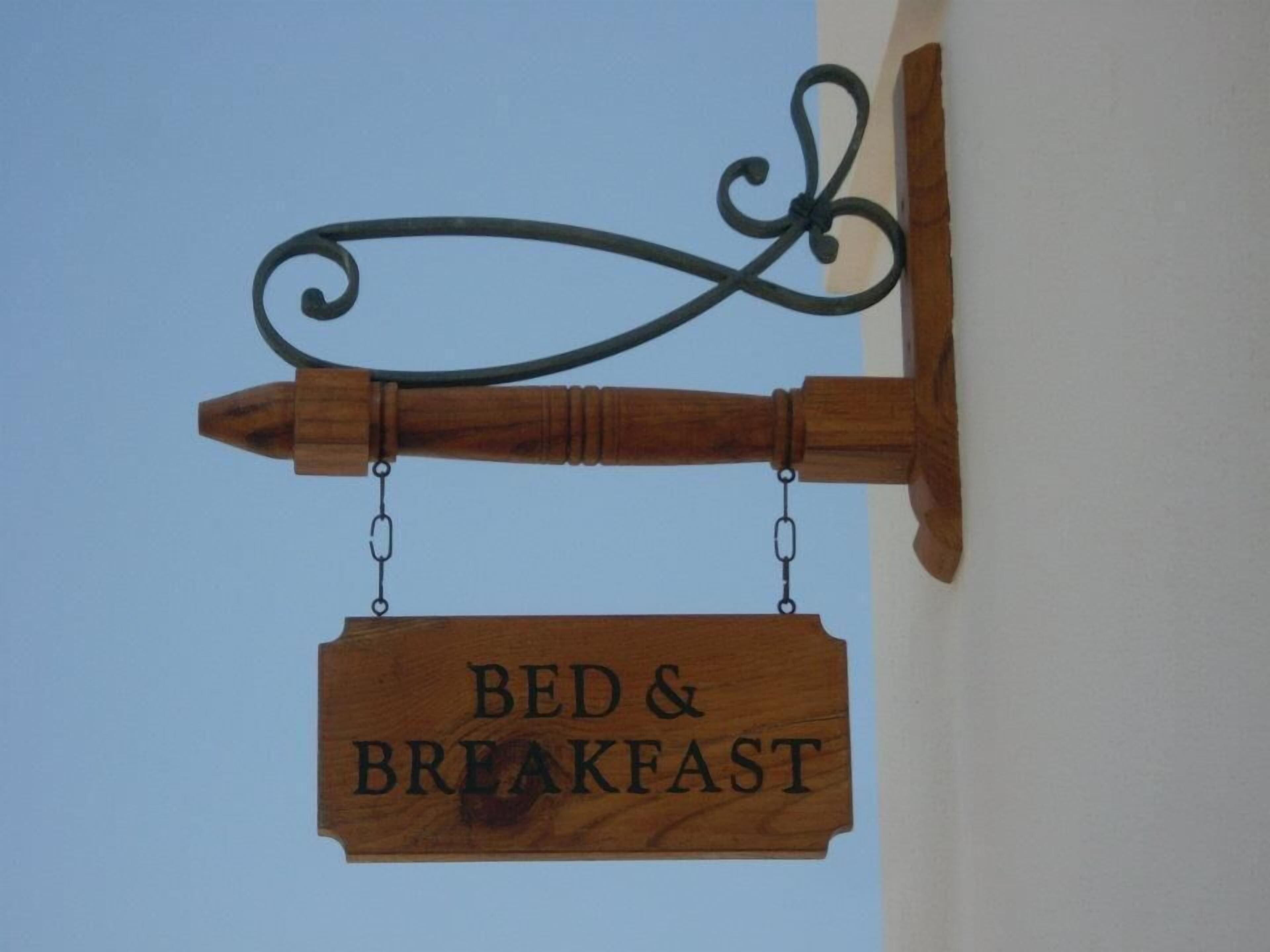 Un letrero de madera con el texto 'BED & BREAKFAST' colgado de una estructura metálica.