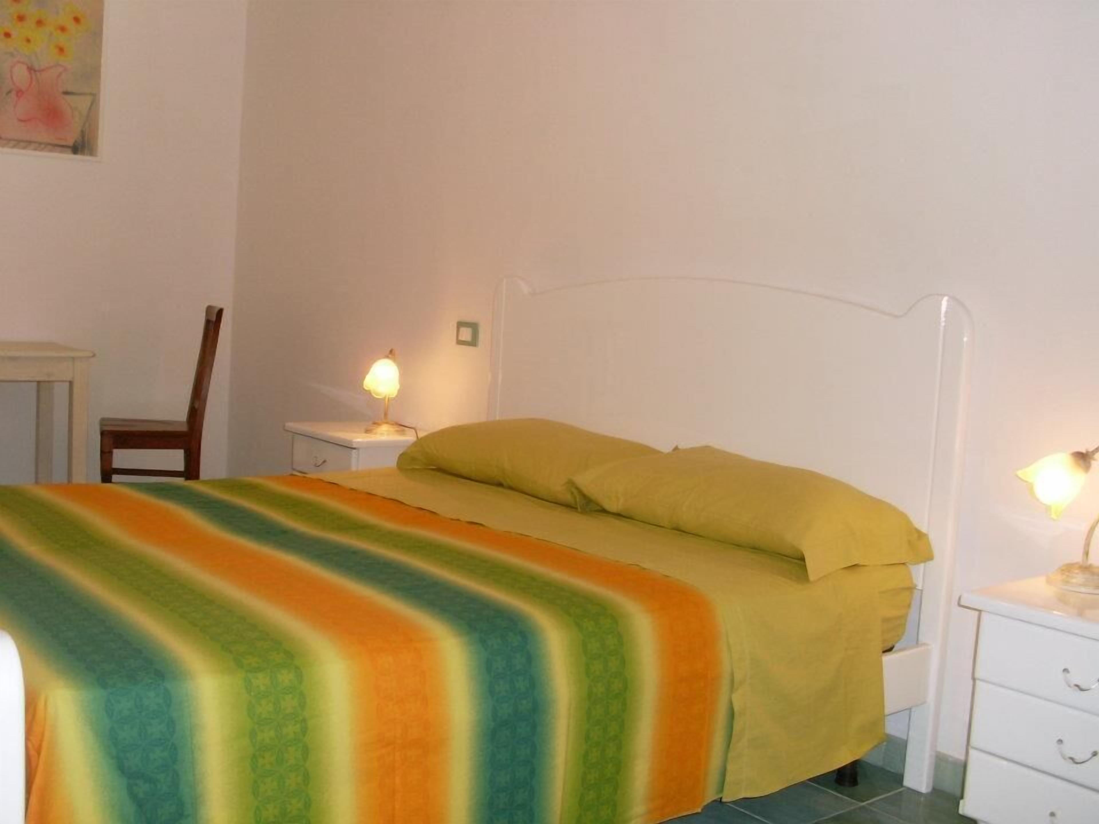 Ein schlichter, sauberer Raum mit einem Bett, einem Sessel, einem Nachttisch mit Lampe und einem kleinen Tisch.