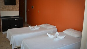 A hotel room with two beds, each with a white bedspread and pillows, and a flat-screen TV mounted on a brick wall. - Residencial Baleia Franca (Florianópolis)