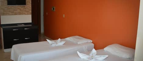 A hotel room with two beds, each with a white bedspread and pillows, and a flat-screen TV mounted on a brick wall.