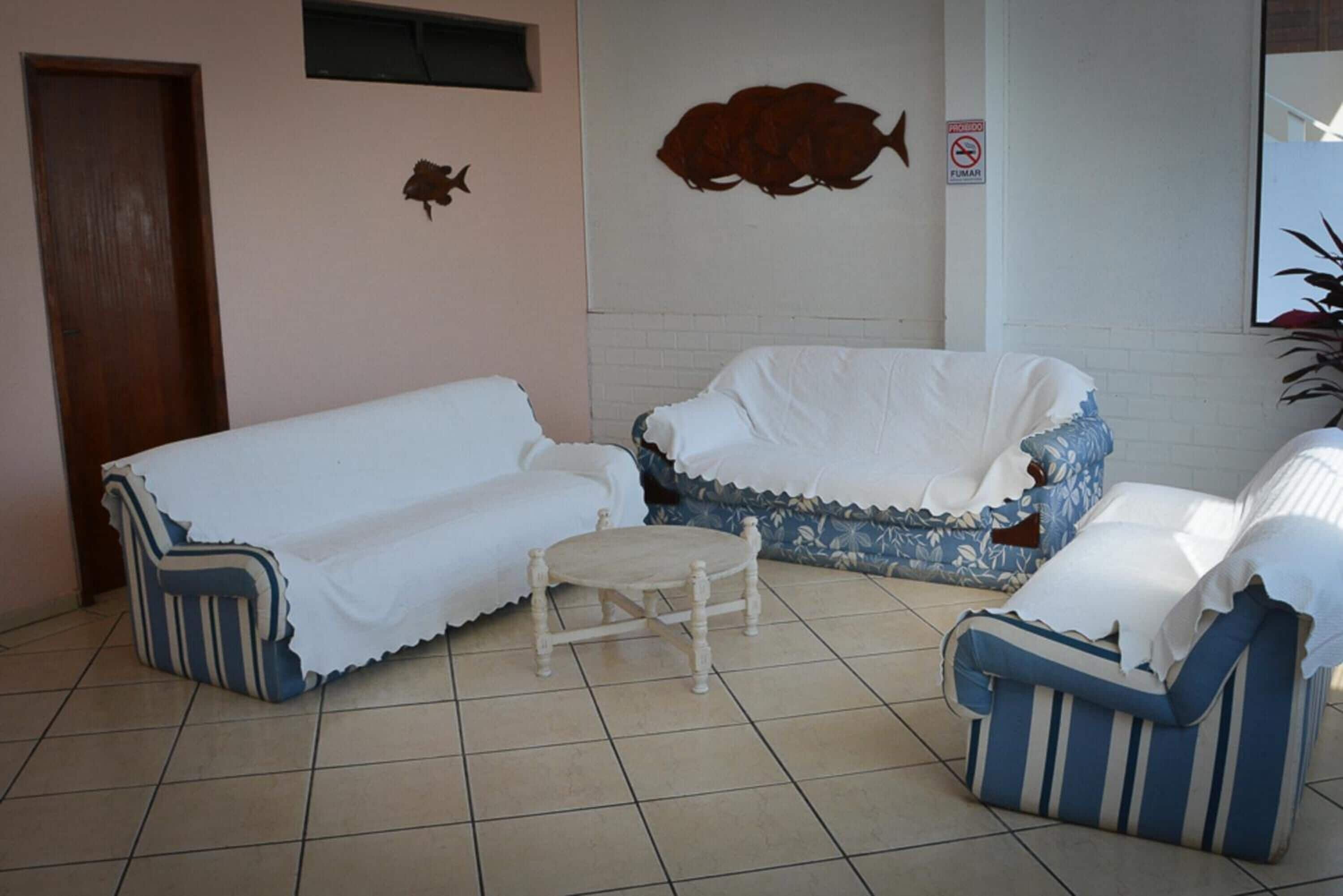 A room with a white sofa, a blue and white striped chair, and a small wooden stool.