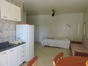 A compact room with a kitchenette, a bed, a ceiling fan, and a floral sofa. - Residencial Baleia Franca (Florianópolis)