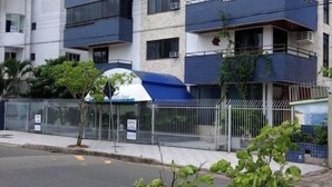 A multi-story building with balconies, a fenced area, and a tree in the foreground. - Residencial Baleia Franca (Florianópolis)
