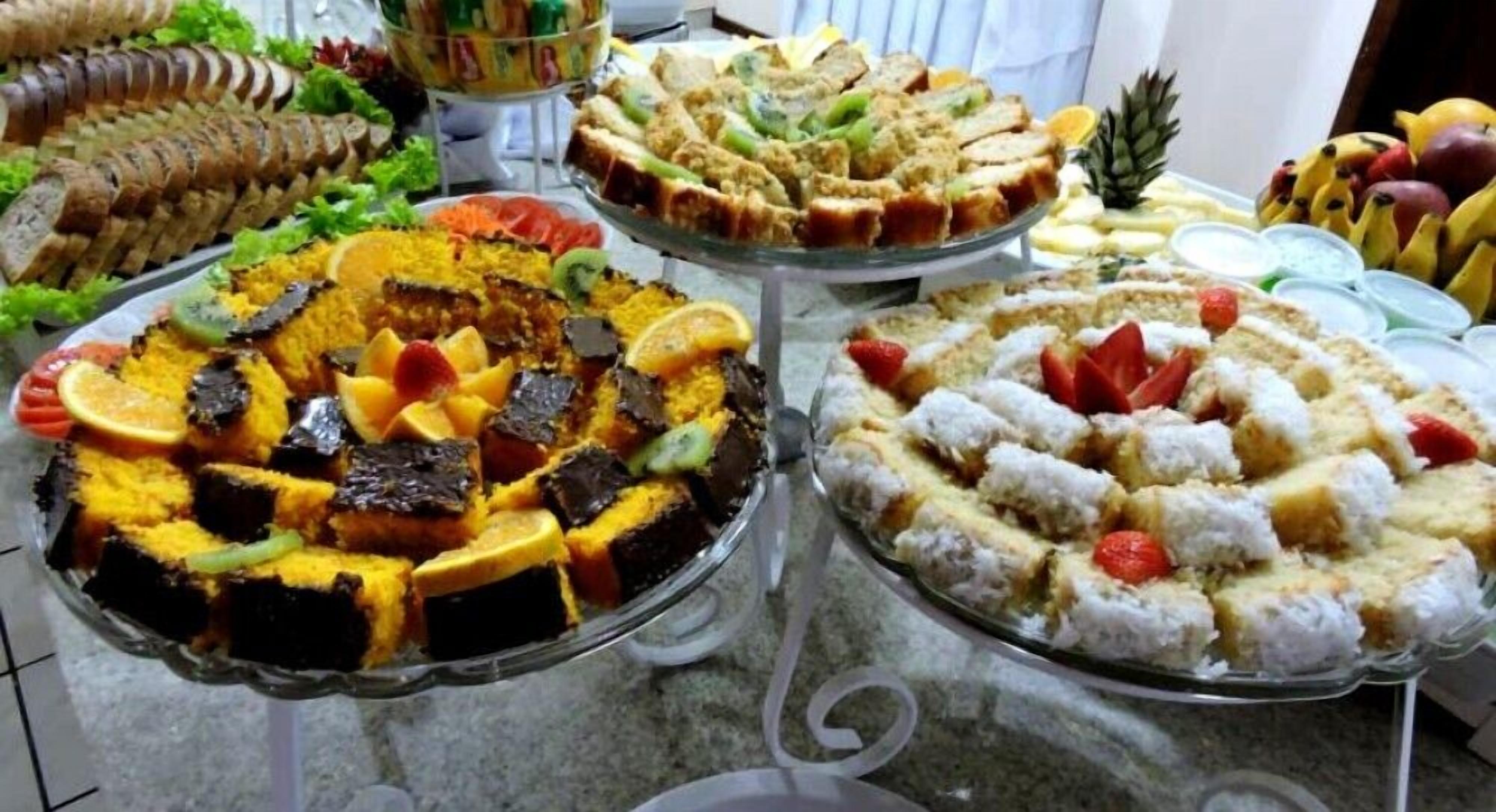 Un bufé con diversos platos, incluyendo un pastel grande con fruta, un pastel en capas y un postre con coco.