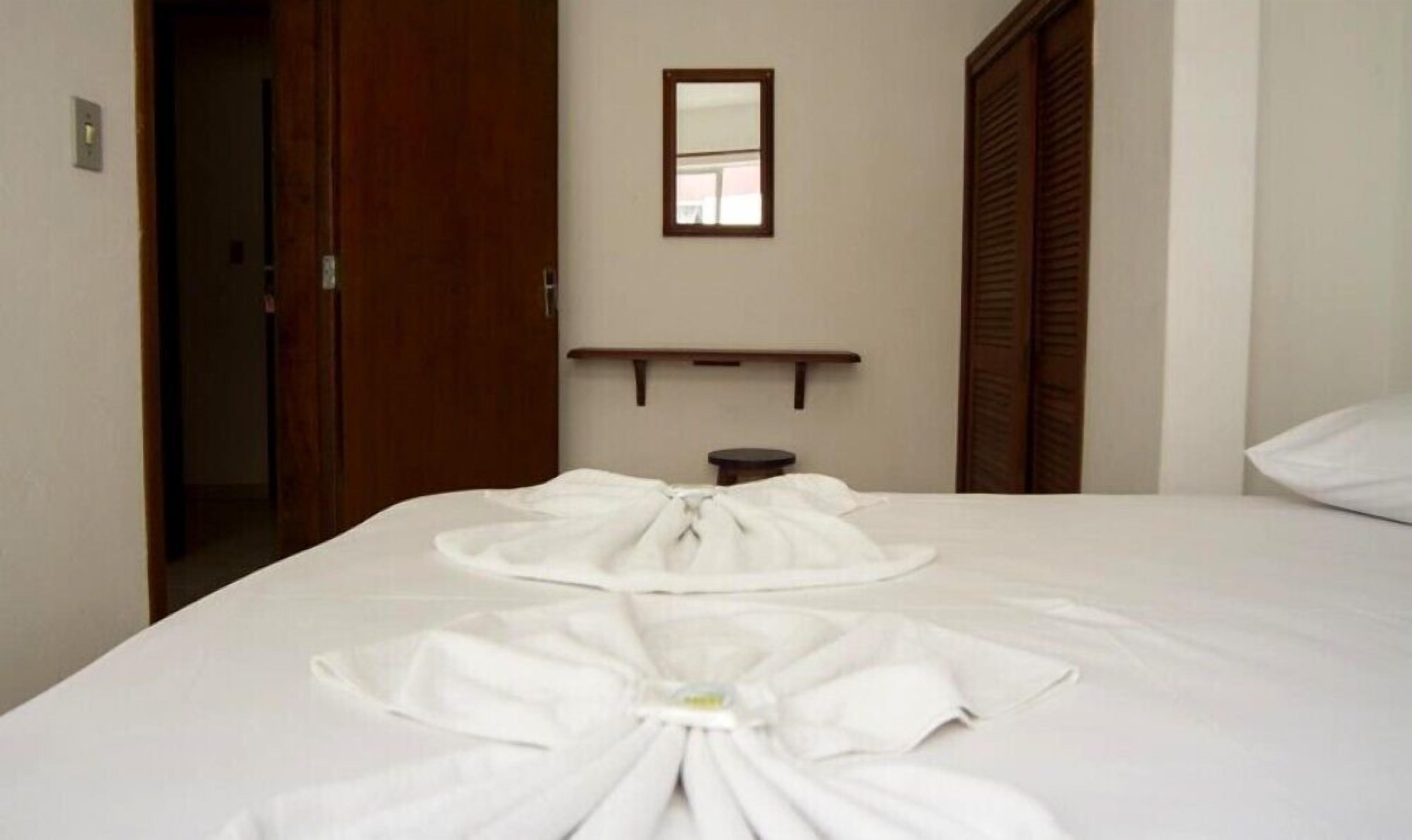 A hotel room with a neatly made bed, a small bedside table, a mirror on the wall, and a wooden door.
