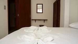 A hotel room with a neatly made bed, a small bedside table, a mirror on the wall, and a wooden door. - Residencial Buenos Aires (Florianópolis)