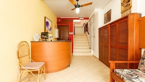 A reception area with a wooden desk, a wicker chair, a sofa, and a staircase leading to an upper floor. - Residencial Buenos Aires (Florianópolis)