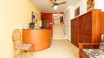 A reception area with a wooden desk, a wicker chair, a sofa, and a staircase leading to an upper floor.