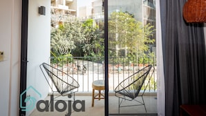 A balcony with two black wire chairs and a small stool, overlooking a courtyard with trees and a building in the background. - Zendero Tulum (Tulum)