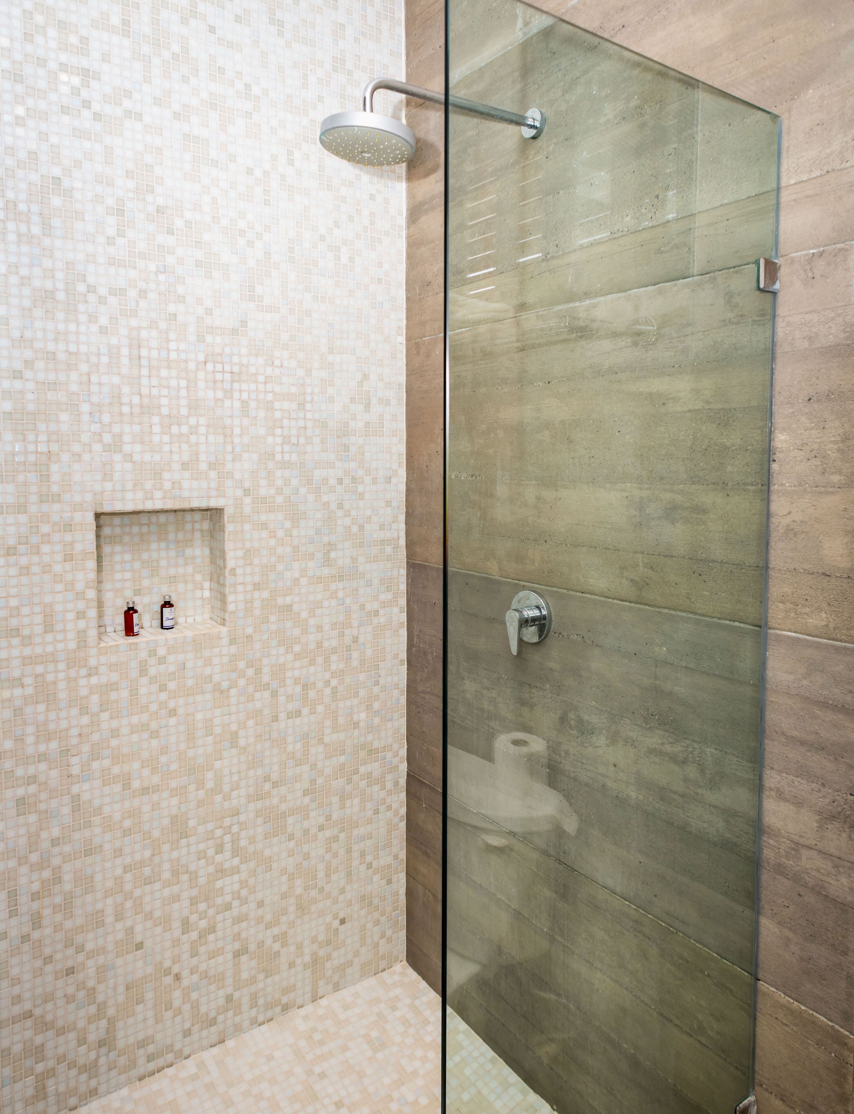 A glass-enclosed shower area with a tiled wall and a small shelf with toiletries.