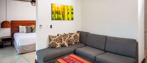 A modern living room with a grey sofa, a wooden coffee table, and a bed with a white duvet.