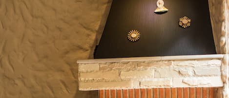 A stone fireplace with a black mantel and decorative sun motifs. A woven tapestry hangs above the fireplace, depicting a landscape scene.
