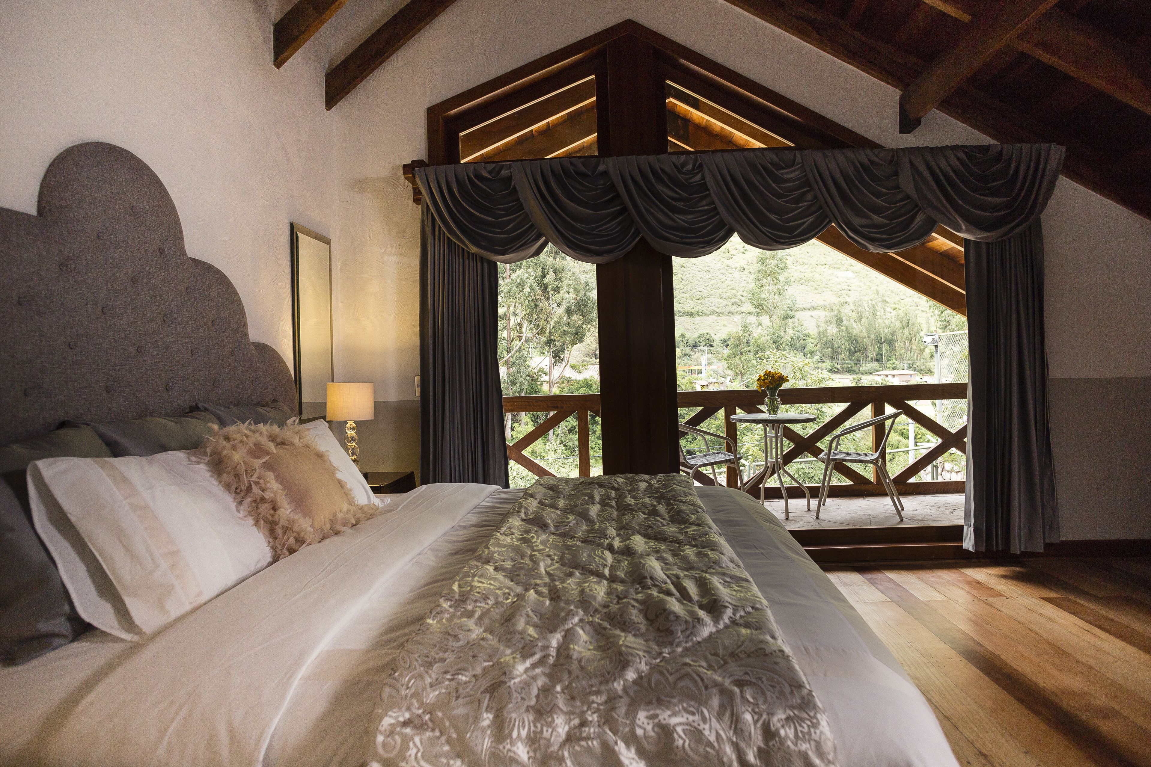 Une chambre avec un grand lit, un plafond en bois et un balcon équipé d’une table et de chaises.