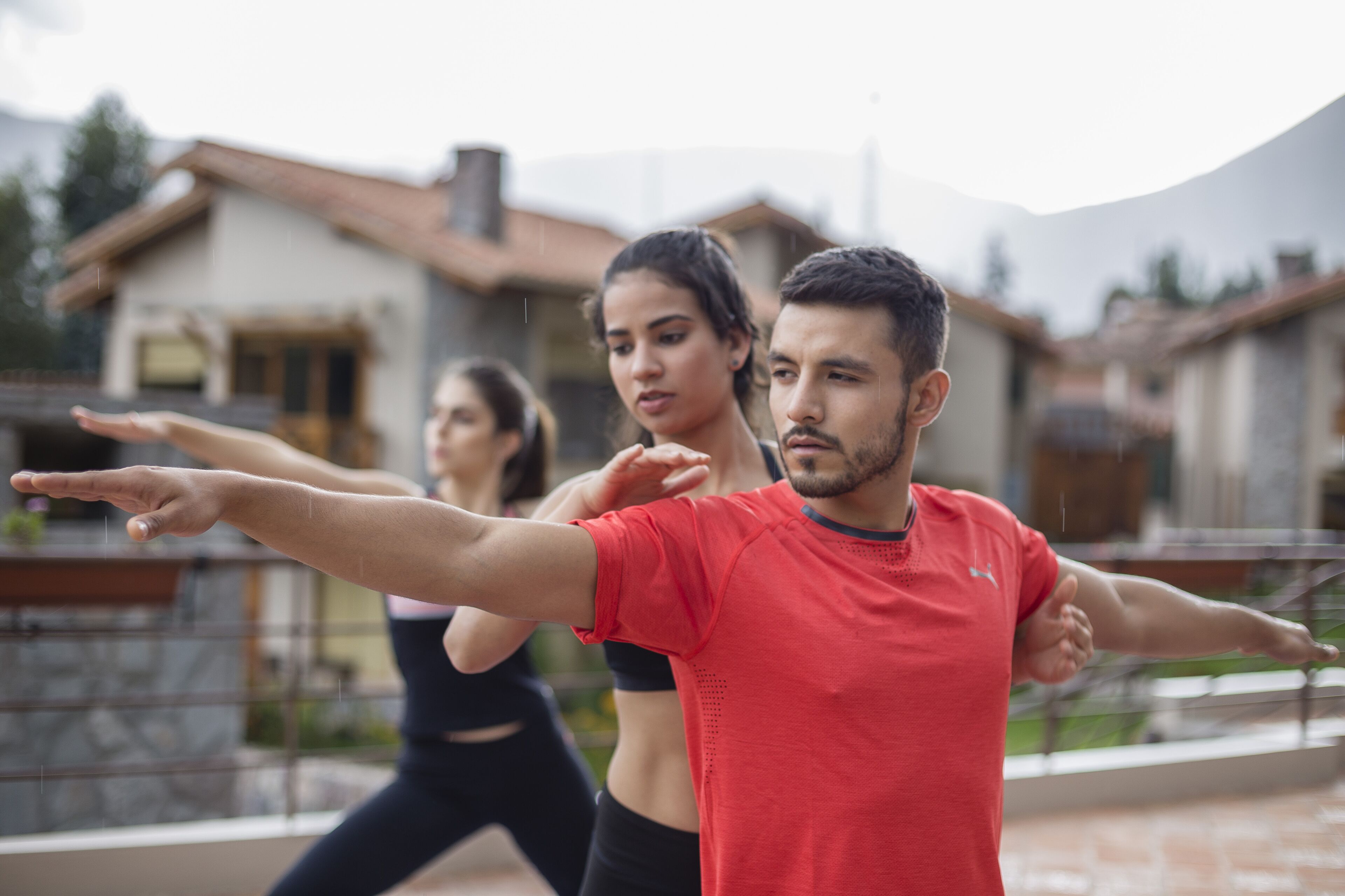 A person in a red shirt and black pants performing an exercise outdoors with a house in the background.
