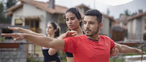 A person in a red shirt and black pants performing an exercise outdoors with a house in the background.